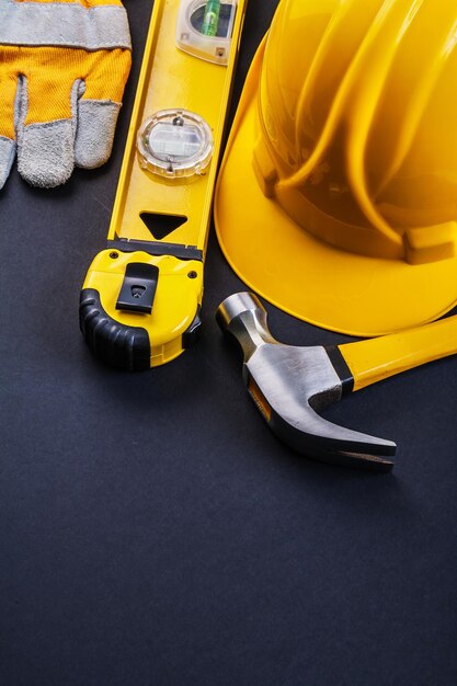 Samenstelling van gele werkinstrumenten klauw hamer tape lijn constructie niveau beschermende handschoen helm op zwarte achtergrond