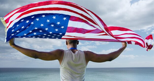 Foto samenstelling van mannelijke atleet die amerikaanse vlag zwaait tegen stormachtige lucht en kust