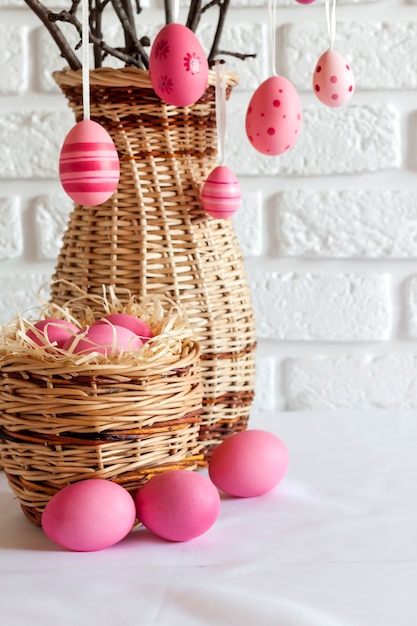Samenstelling van pasen met versierde boomtakken in een rieten vaas en roze gekleurde eieren in rieten mand
