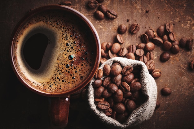Samenstelling van vers gezette kop koffie en gebrande koffiebonen in zak op bruine achtergrond