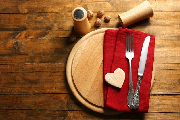 Samenstelling van vork mes servet en decoratieve harten op snijplank op houten tafel achtergrond