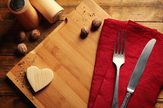 Samenstelling van vork mes servet en decoratieve harten op snijplank op houten tafel achtergrond