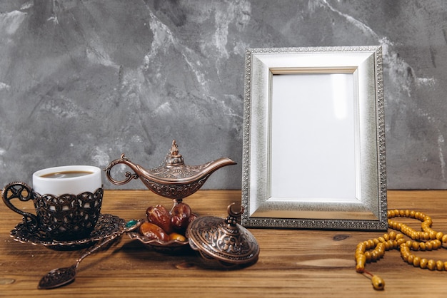 Samenstelling voor Ramadan Zilveren frame met kopieerruimte of mockup in de buurt van traditioneel islamitisch servies met dadels en koffie op houten tafel