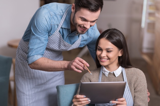 Samenwerken. Geïnspireerd blij paar koffie-eigenaren die glimlachen en tablet gebruiken terwijl ze rusten.