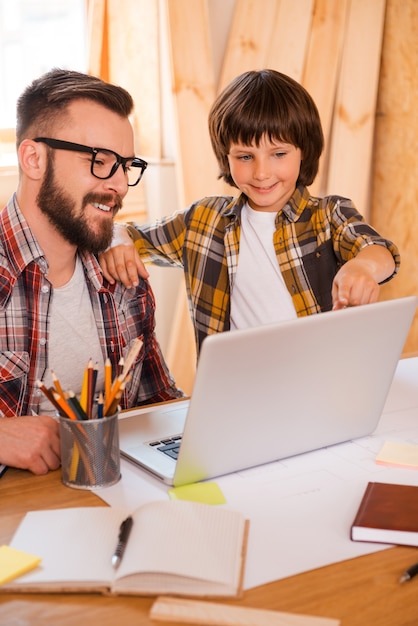 Samenwerken met vader. Gelukkig jonge man aan het werk op laptop terwijl zijn zoontje erop wijst