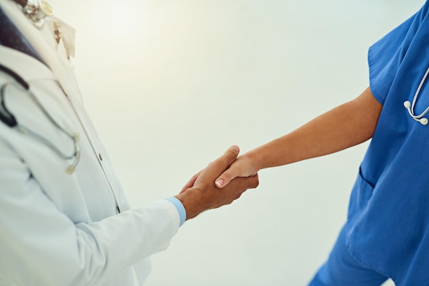 Samenwerking gaat een lange weg in de geneeskunde Hoge hoekopname van twee niet-identificeerbare zorgverleners die elkaar de hand schudden in de foyer van het ziekenhuis