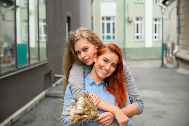 Samesex relationships Happy lesbian couple with dried flowers The girl gently hugs the redhaired girlfriend from behind Close up to a pair of hands LGBT