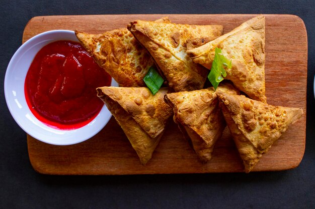 Samosa samsa or somsa are triangular fried pastries or pastri served with tomato sauce and leek slice on black background