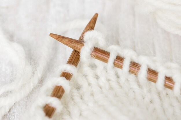 Sample of knitting from woolen yarn white color on wooden knitting needles on a wooden background