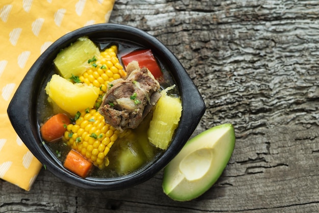 Photo sancocho typical colombian food in a black bowl on a rustic wooden background