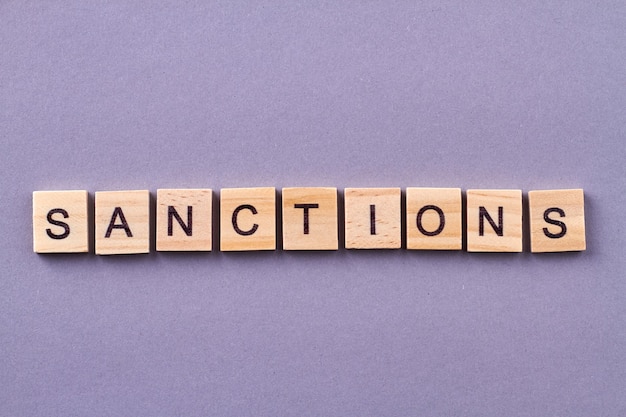 Sanctions word made of wooden cubes. Isolated on purple background.