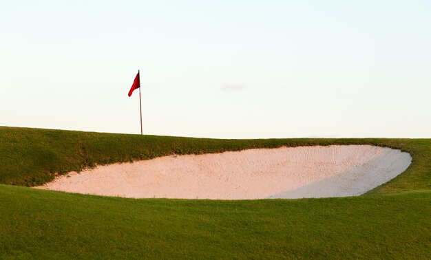 Sand bunker in front of golf green and flag