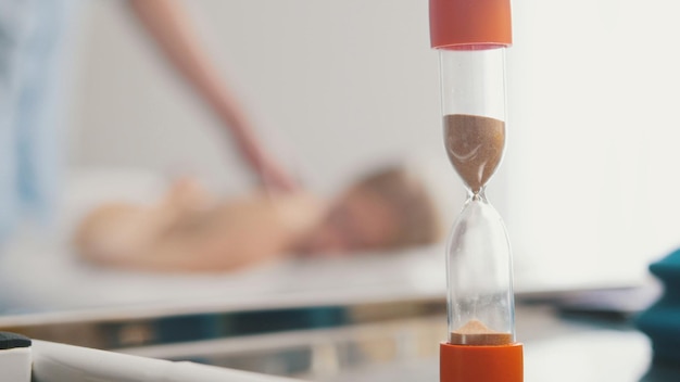 Sand clock in cabinet of tibetan medicine - massage for young blonde woman, blurred