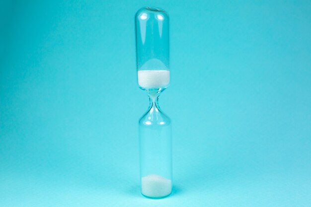 Sand clock on turquoise background. Hourglass as time passing concept. Close up photo.