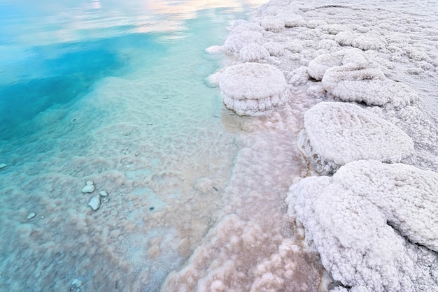 Sand completely covered with crystalline salt on shore of Dead Sea, turquoise blue water near - typical scenery at Ein Bokek beach, Israel