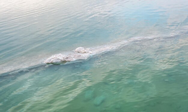 Sand covered with crystalline salt on shore of Dead Sea, clear calm water near - typical scenery at Ein Bokek beach, Israel