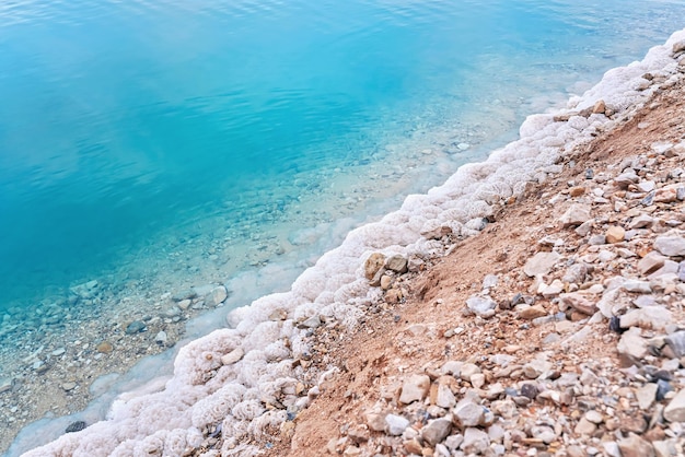 Sand covered with crystalline salt on shore of Dead Sea, turquoise blue water near - typical scenery at Ein Bokek beach, Israel