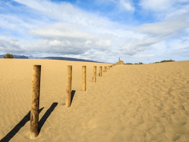 Sand in the Dunes of Maspalomas, a small desert on Gran Canaria. Sand and sky, and a wooden fence marking the forbidden area of the bird nature reserve La Charca.