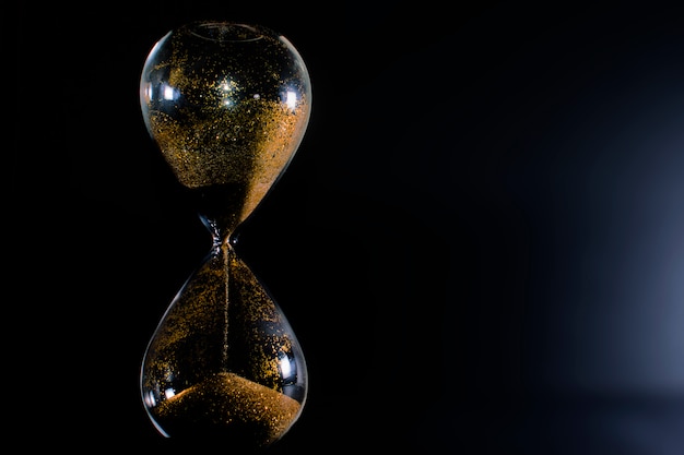 Sand and golden glitter passing through the glass bulbs of an hourglass.