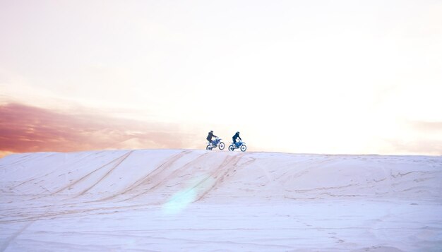 写真 砂の自然、またはアクションアドベンチャーやパフォーマンスやアドレナリンを伴うフィットネスのためにバイクを運転する人々 チームワークの砂漠、またはトレーニング演習やレースチャレンジのために砂丘でバイクに乗るアスリート