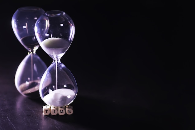 Sand running through the bulbs of an hourglass measuring the\
passing time in a countdown to a deadline, on a dark table\
background with copy space.