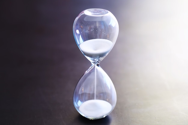 Sand running through the bulbs of an hourglass measuring the passing time in a countdown to a deadline, on a dark table background with copy space.