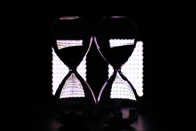 Sand running through the bulbs of an hourglass measuring the passing time in a countdown to a deadline, on a dark table background with copy space.