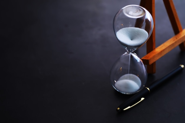 Sand running through the bulbs of an hourglass measuring the passing time in a countdown to a deadline, on a dark table background with copy space.