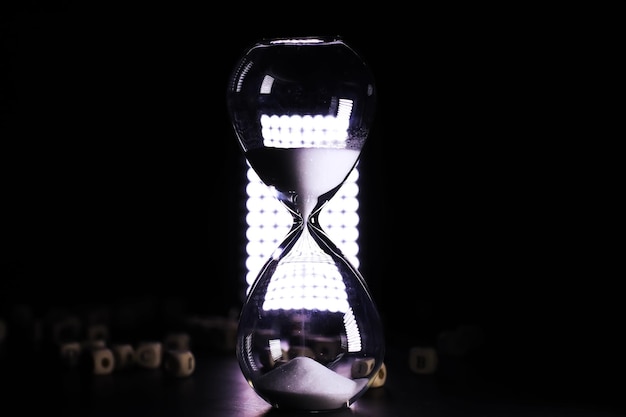 Sand running through the bulbs of an hourglass measuring the\
passing time in a countdown to a deadline on a dark table\
background with copy space