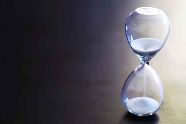 Sand running through the bulbs of an hourglass measuring the passing time in a countdown to a deadline on a dark table background with copy space