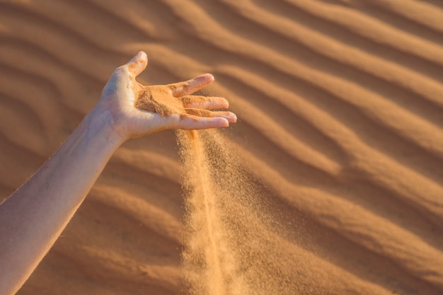 Sand slipping through the fingers of a woman's hand in the desert.