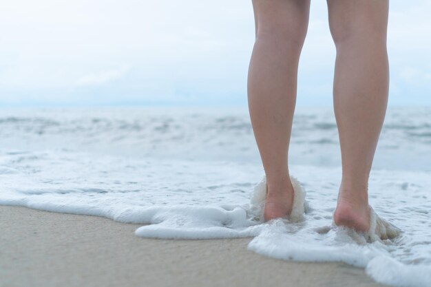 푸른 하늘을 배경으로 한 모래 열대 해변에서 여성의 발은 천천히 걸으며 휴식을 취합니다