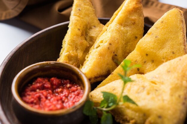 Sandwich Bread Pakora or pakoda (triangle shape) served  with tomato ketchup, chutney, green chilli  and onion slices, Popular indian  tea-time snack. Selective focus