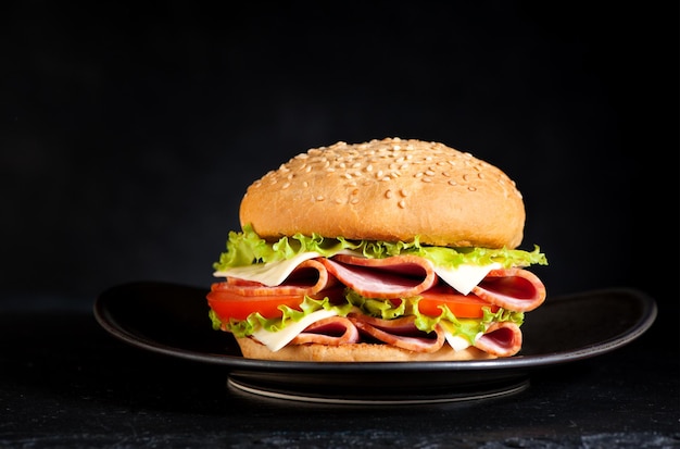 Сэндвич-бургер с ветчиной, сыром и овощами на черном фоне