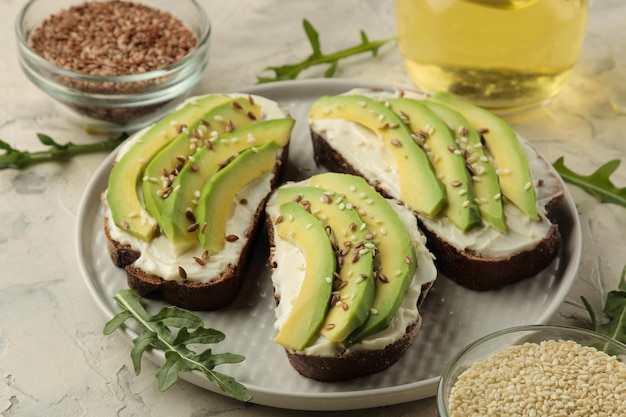 A sandwich of cream cheese bread and slices of avocado on a plate on a light concrete background making sandwiches