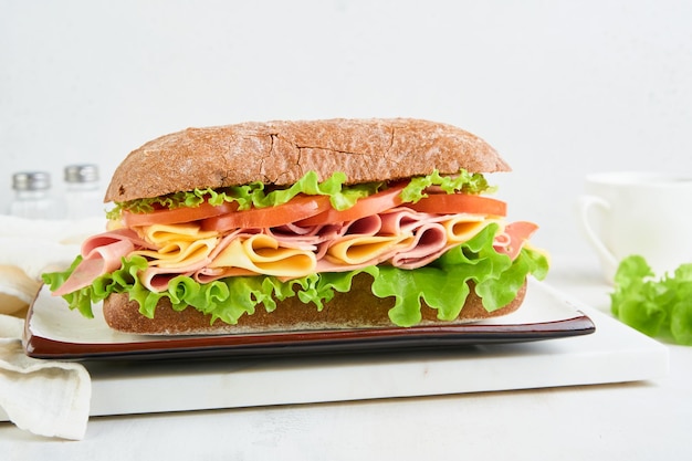 Sandwich Eén verse grote onderzeeër sandwich met ham kaas sla tomaten en microgreens op lichte achtergrond Gezond ontbijt thema concept school lunch ontbijt of snack