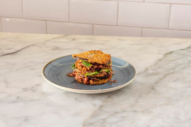 Photo sandwich of fried aubergine slices presented in layers with chicken pull filling and vegetables on marble table