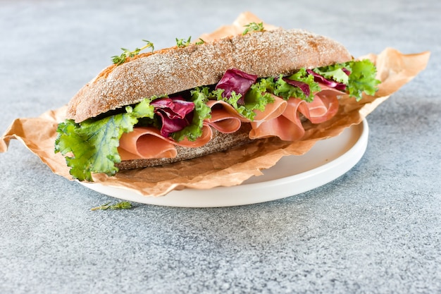 Sandwich from a cereal baguette  prosciutto, lettuce, kale on a gray background