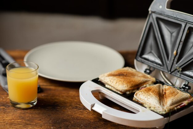 Sandwich and juice Snack and breakfast preparation Sandwich maker and empty plate on wooden background