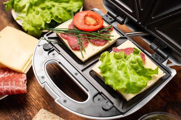 A sandwich maker with two different sandwiches with tomatoes ham onions and cheese Preparing a light meal