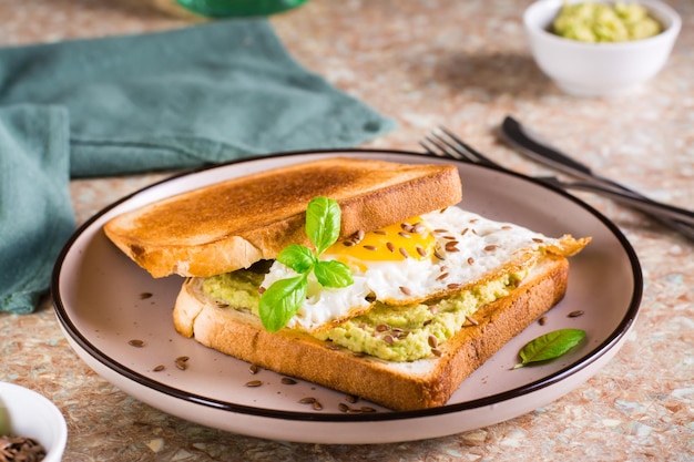 Sandwich met avocado gebakken ei en lijnzaad op toast op een bord op tafel