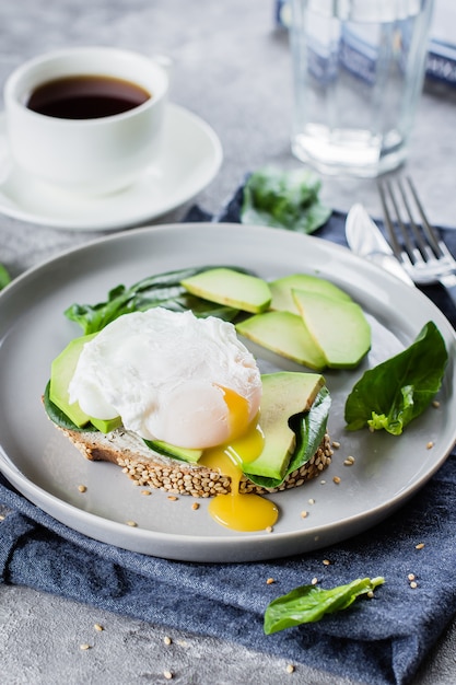 Sandwich met avocado, spinazie en gepocheerd ei op volkoren brood op plaat op stenen rug