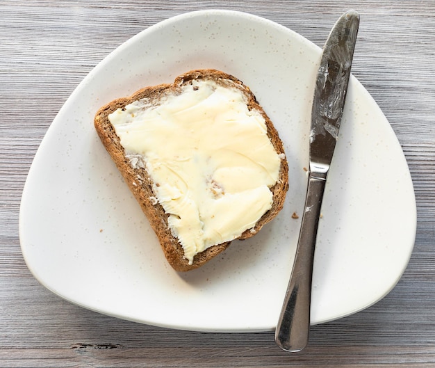 Sandwich met boter en mes op plaat op tafel