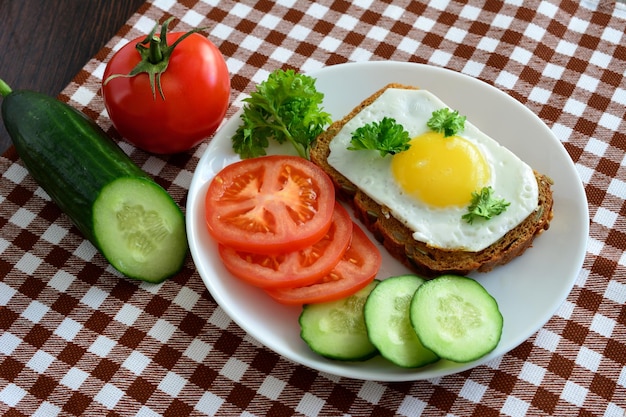 sandwich met gebakken ei op de witte plaat met plakjes tomaat en komkommer