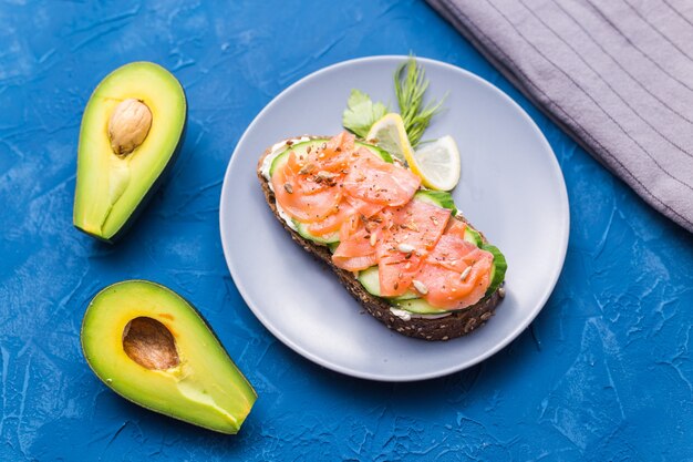 Sandwich met gerookte zalm en komkommer op blauwe achtergrond met avocado, bovenaanzicht. Concept voor