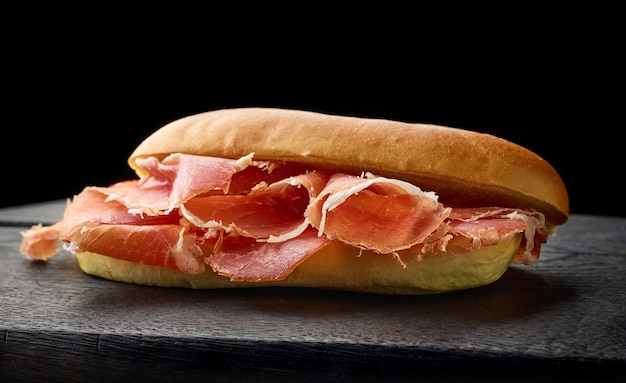 Sandwich met gesneden Spaanse Iberico ham op zwart houten bord