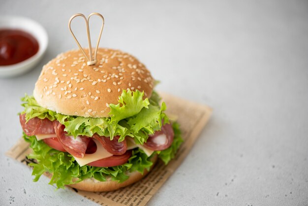 Sandwich met ham, maasdam kaas, tomaten en groene salade op een witte tafel