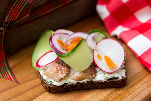 Sandwich met haring, radijs en komkommer op een houten bord