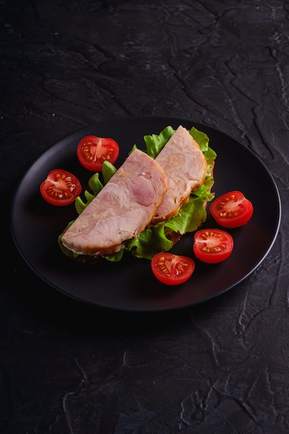 Sandwich met kalkoen ham vlees, groene salade en verse cherrytomaatjes segmenten op zwarte plaat