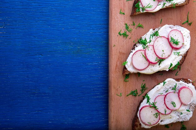 Sandwich met radijskaas aan boord op blauwe houten. Bovenaanzicht copyspace.